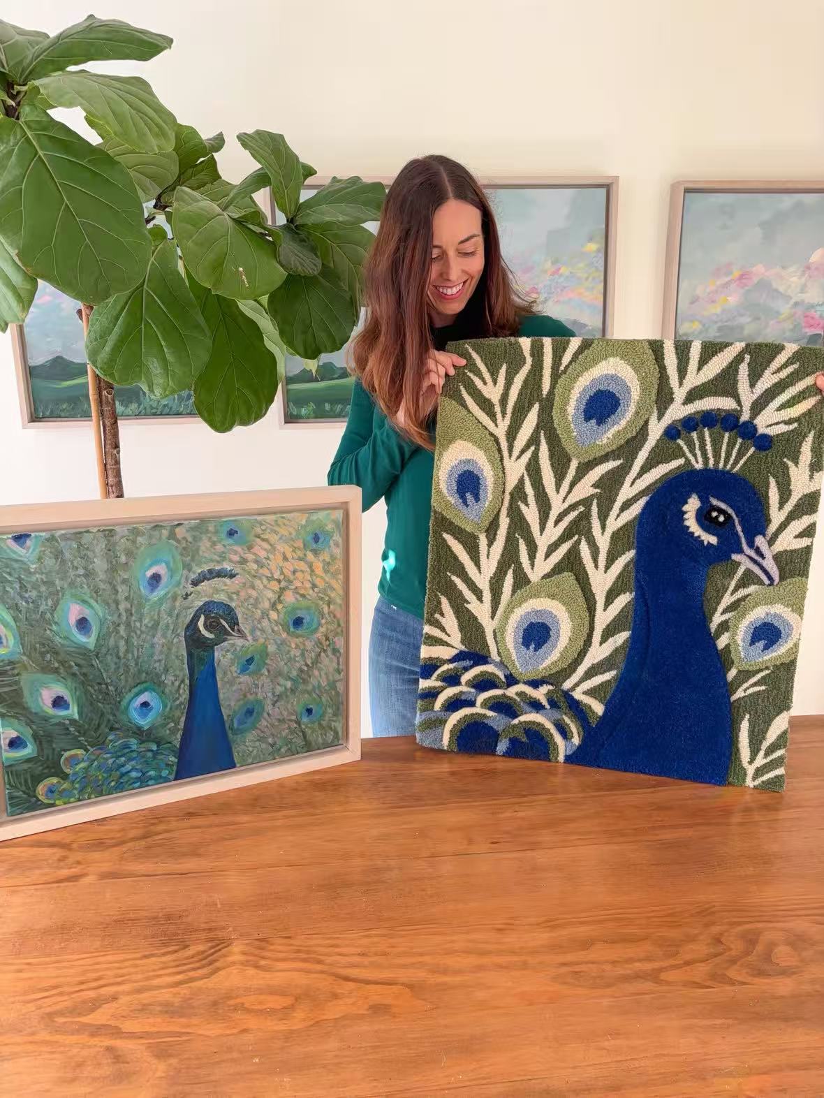 A woman holding a hand-tufted peacock wall hanging beside the original artwork.