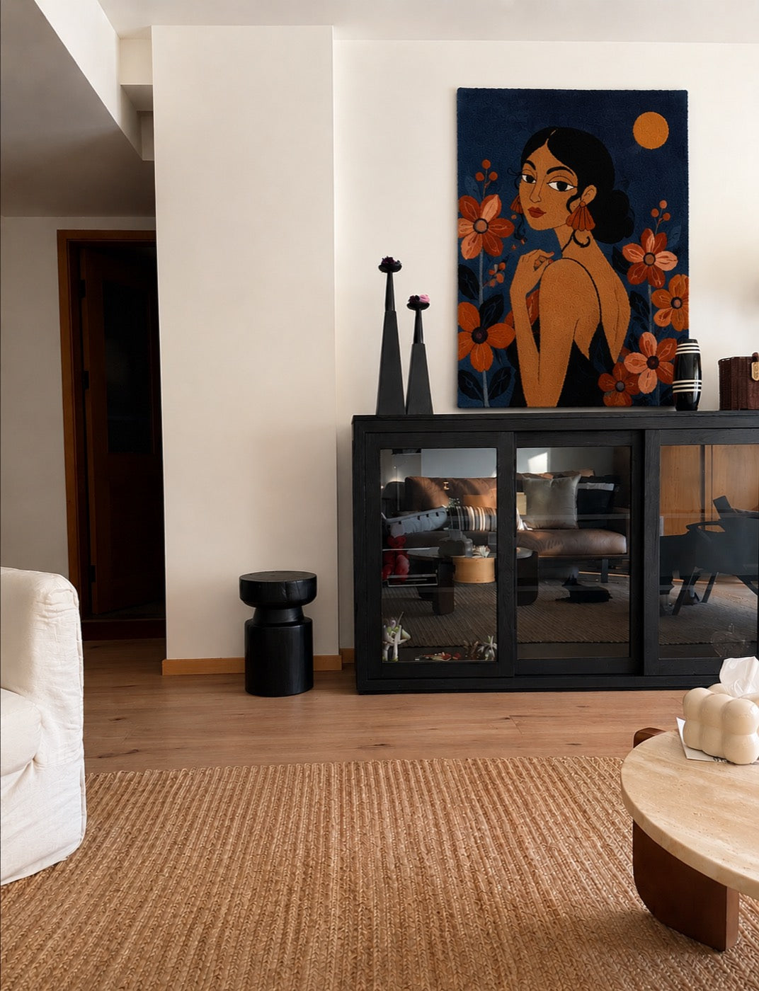 A hand-tufted wool portrait of a woman among rust flowers on deep blue ground, above a black glass cabinet