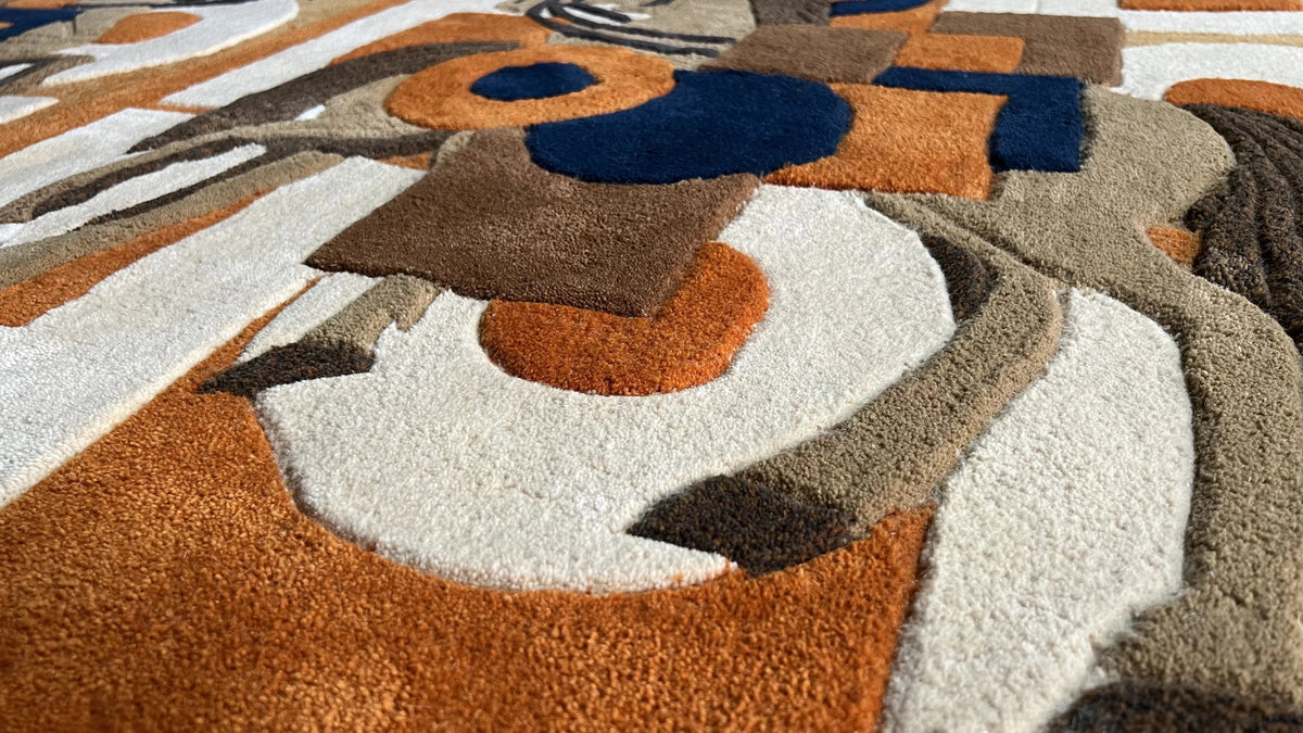 Close-up of a hand-tufted wool tapestry: carved relief in orange, navy, brown and cream