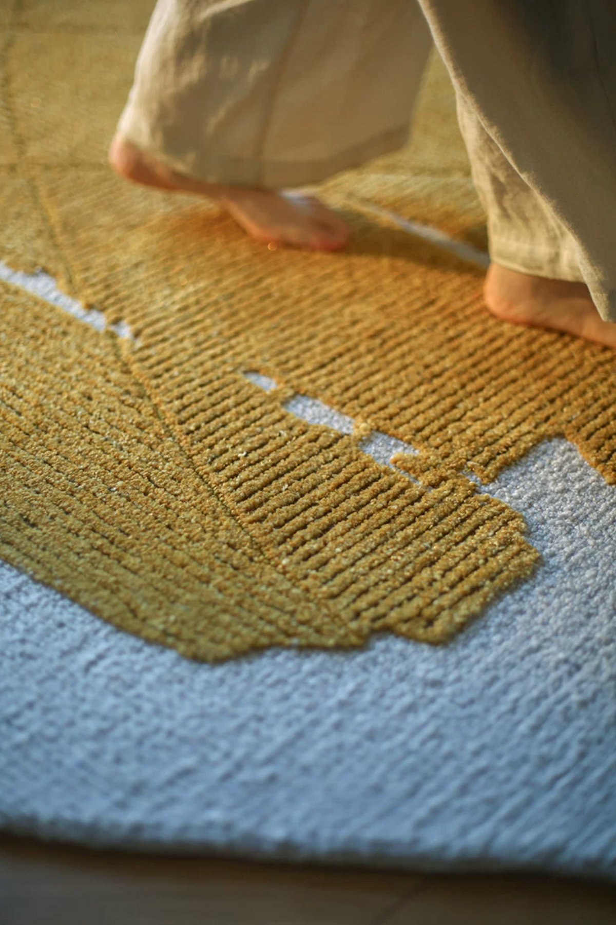 Gold leaf foil rug by Hewn Earth Studio with feet, showcasing a shiny, metallic design on a textured surface.