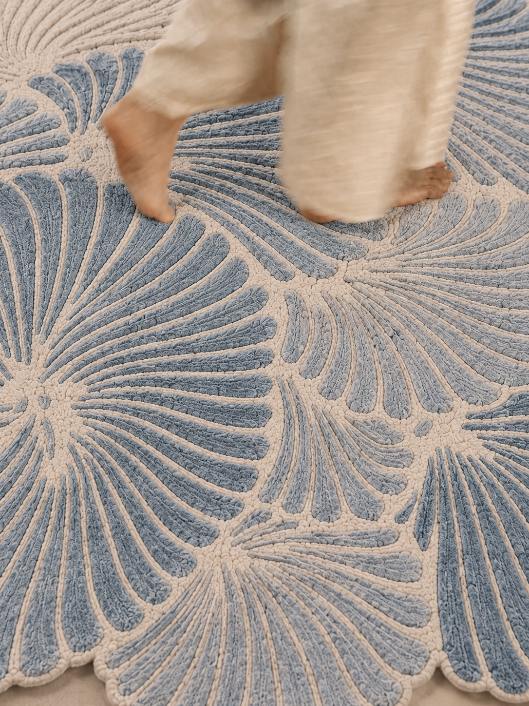 Hewn Earth Studio Frond slate rug featuring a textured, natural design with feet visible on a neutral-colored floor.