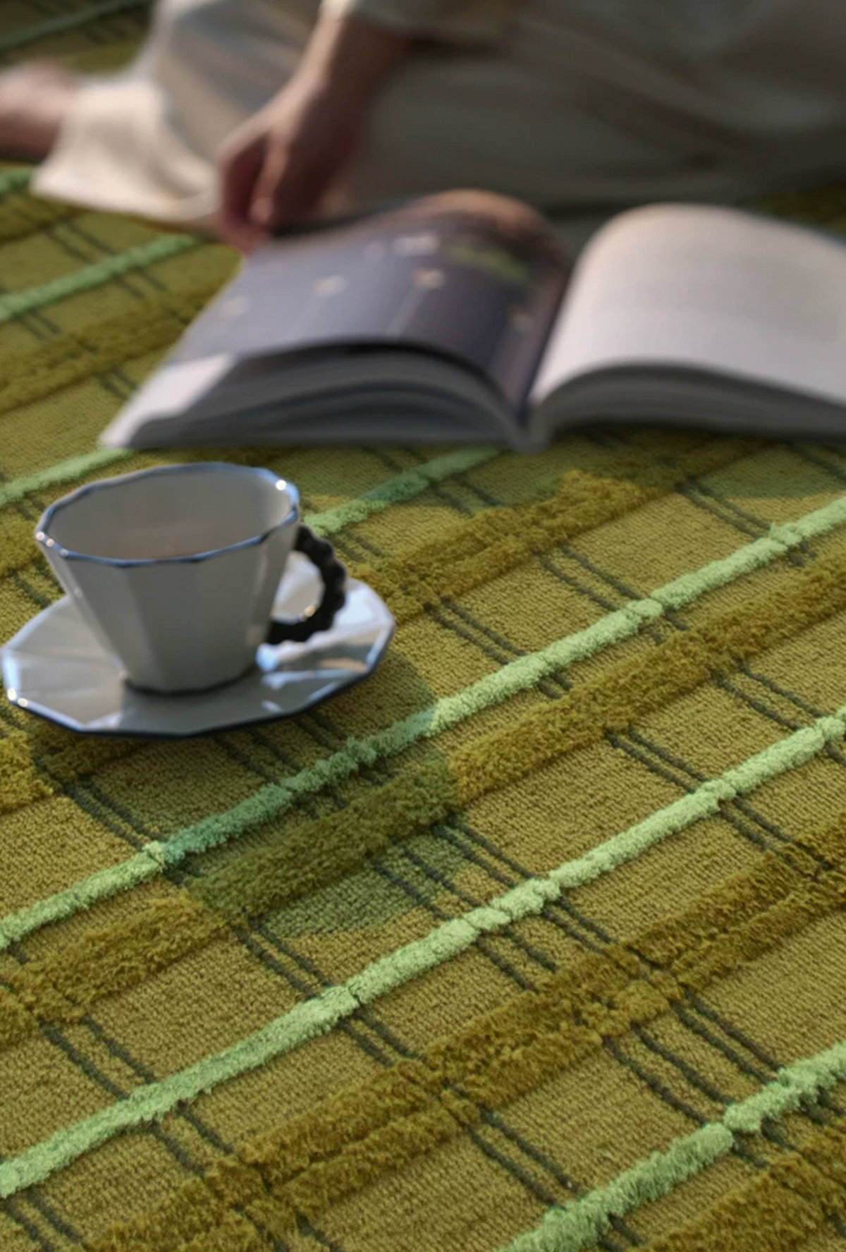 Hewn Earth Studio moss-colored grid rug with geometric pattern on a neutral floor in a modern living space.