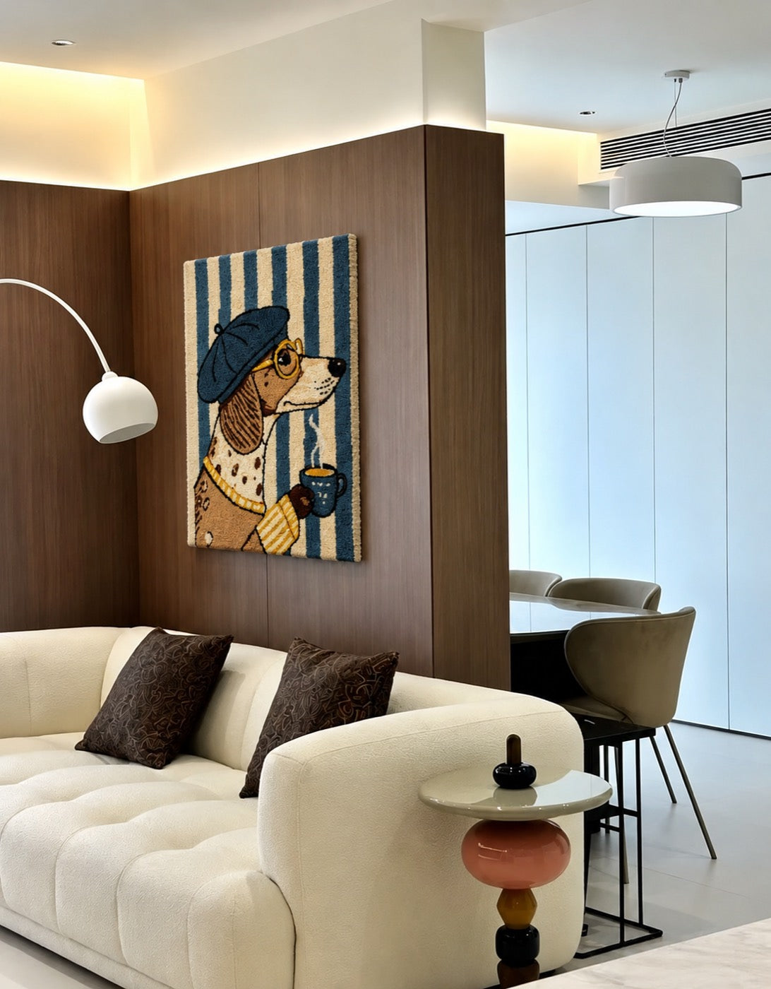 A hand-tufted wool portrait of a dachshund in a blue beret hung on a walnut wall above a bouclé sofa