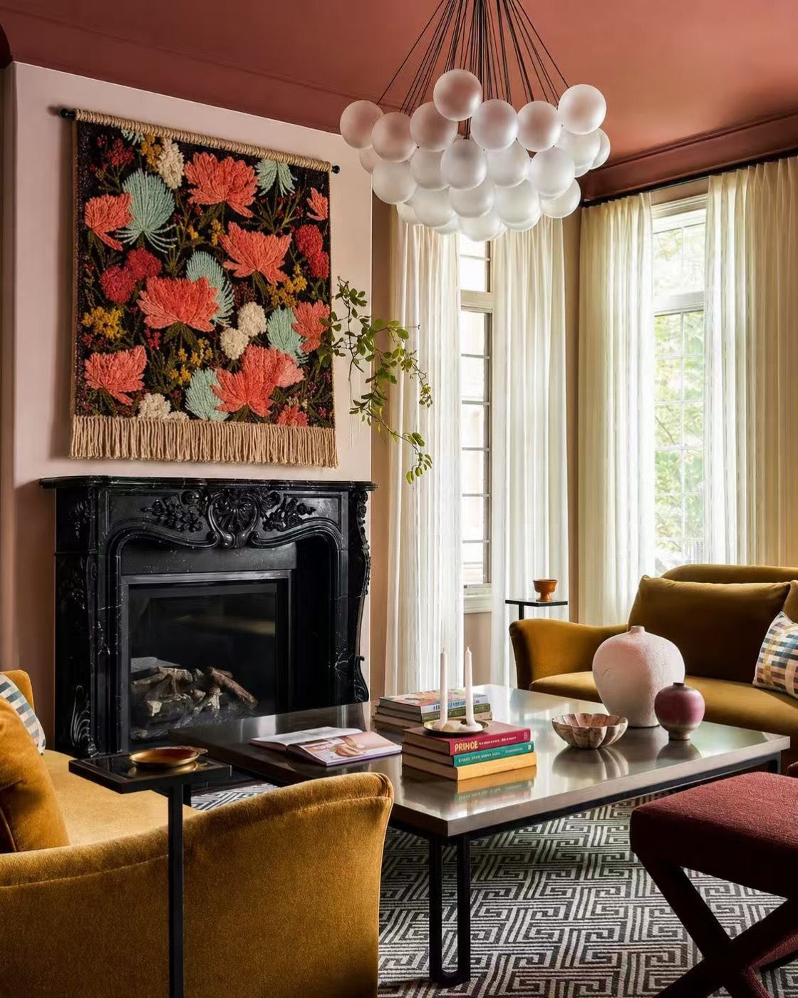 A fringed hand-tufted wool tapestry of coral chrysanthemums hung above a black marble fireplace in a terracotta-ceilinged sitting room