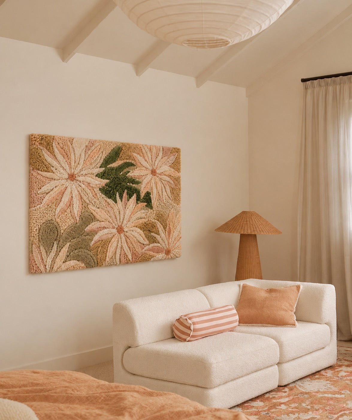 A hand-tufted wool panel of blush and cream daisies hung above a bouclé sofa in a beamed cream bedroom