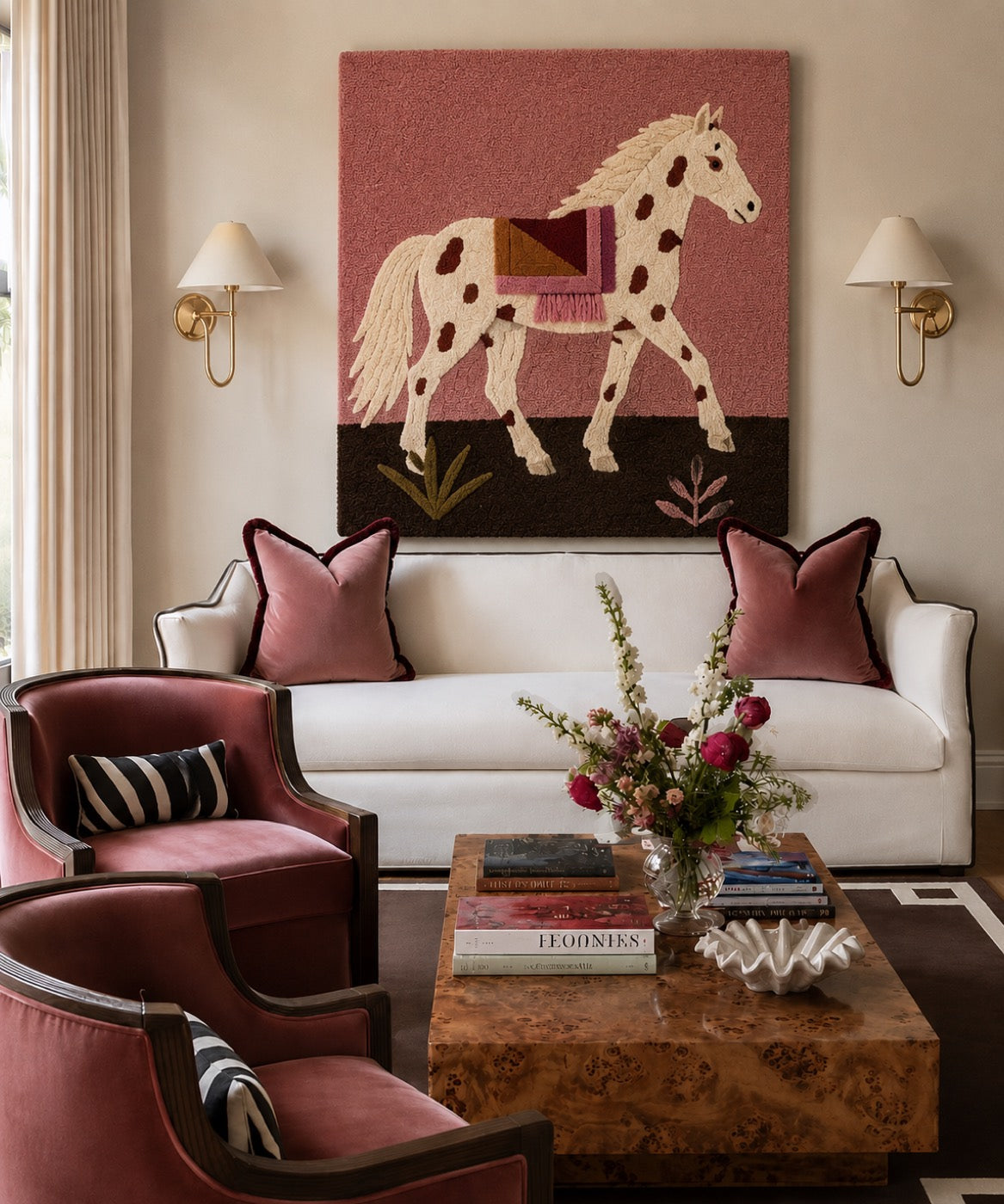 A hand-tufted wool dappled horse panel on a rose ground hung between brass sconces above a white sofa