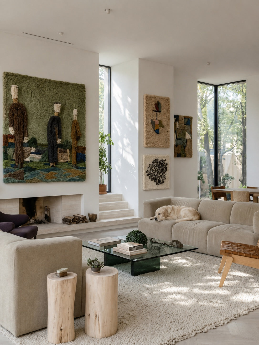 A warm neutral living room with a green woven figures tapestry above the fireplace and abstract textile art on the side wall, a golden retriever on the sofa