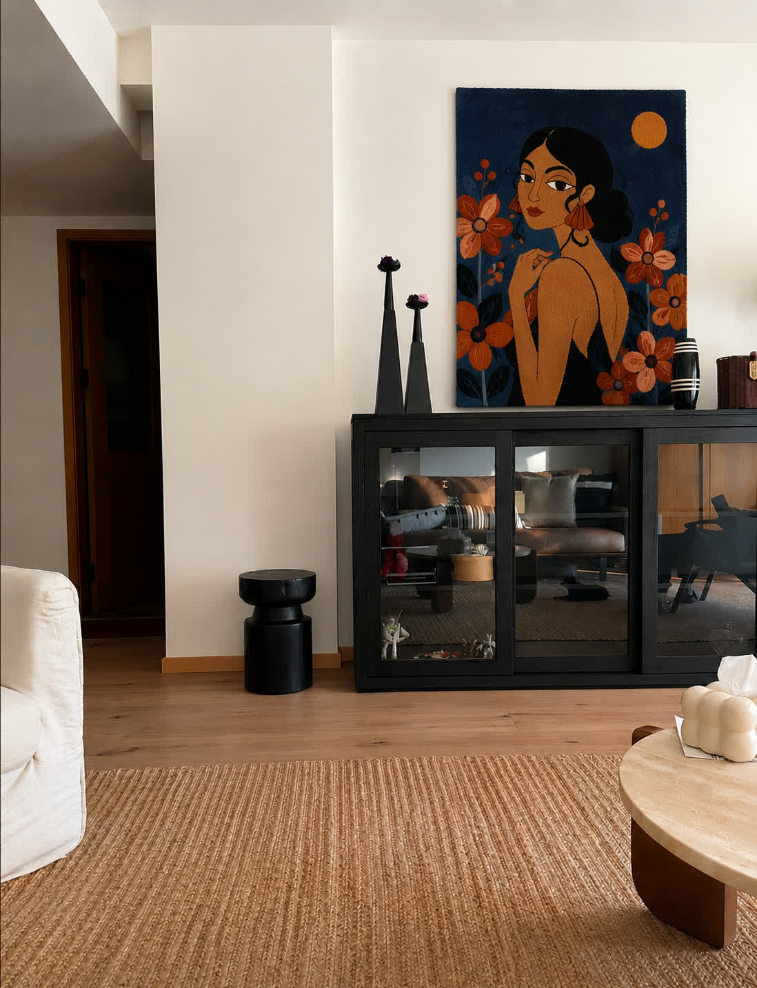 A hand-tufted wool portrait of a woman among rust flowers on deep blue ground, above a black glass cabinet