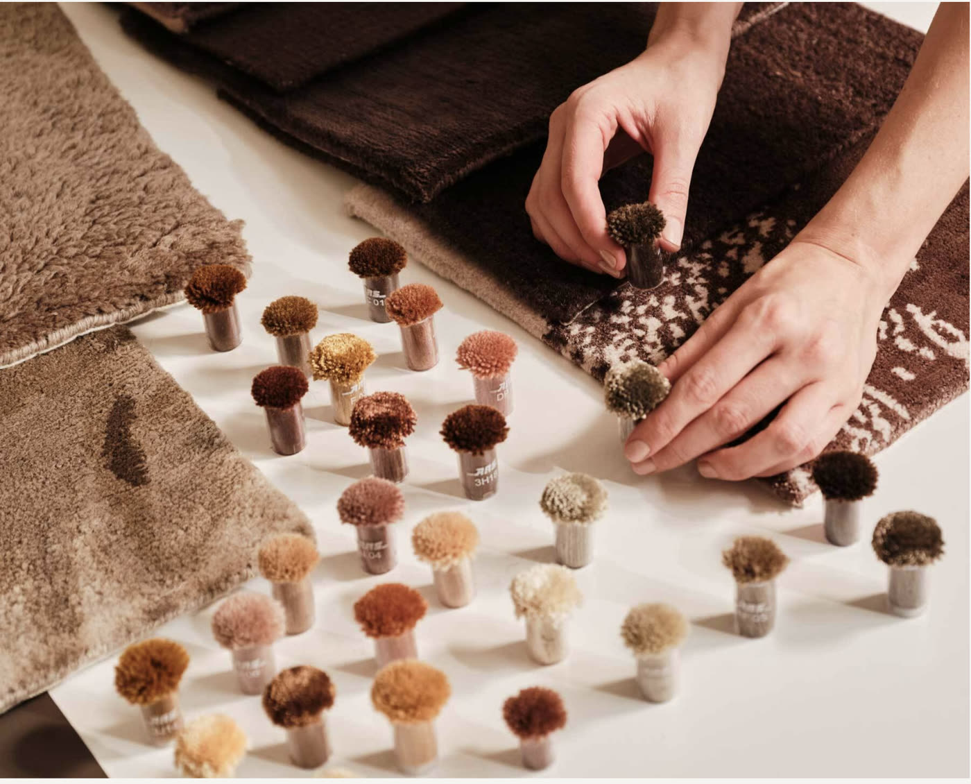 A maker matching wool pom-pom colour samples against woven rug swatches